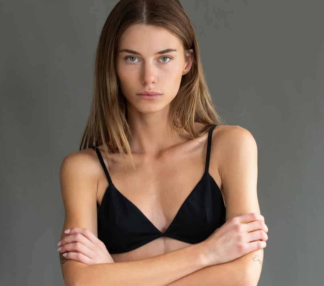 Elegant woman in black top with arms crossed, confident look, gray background.