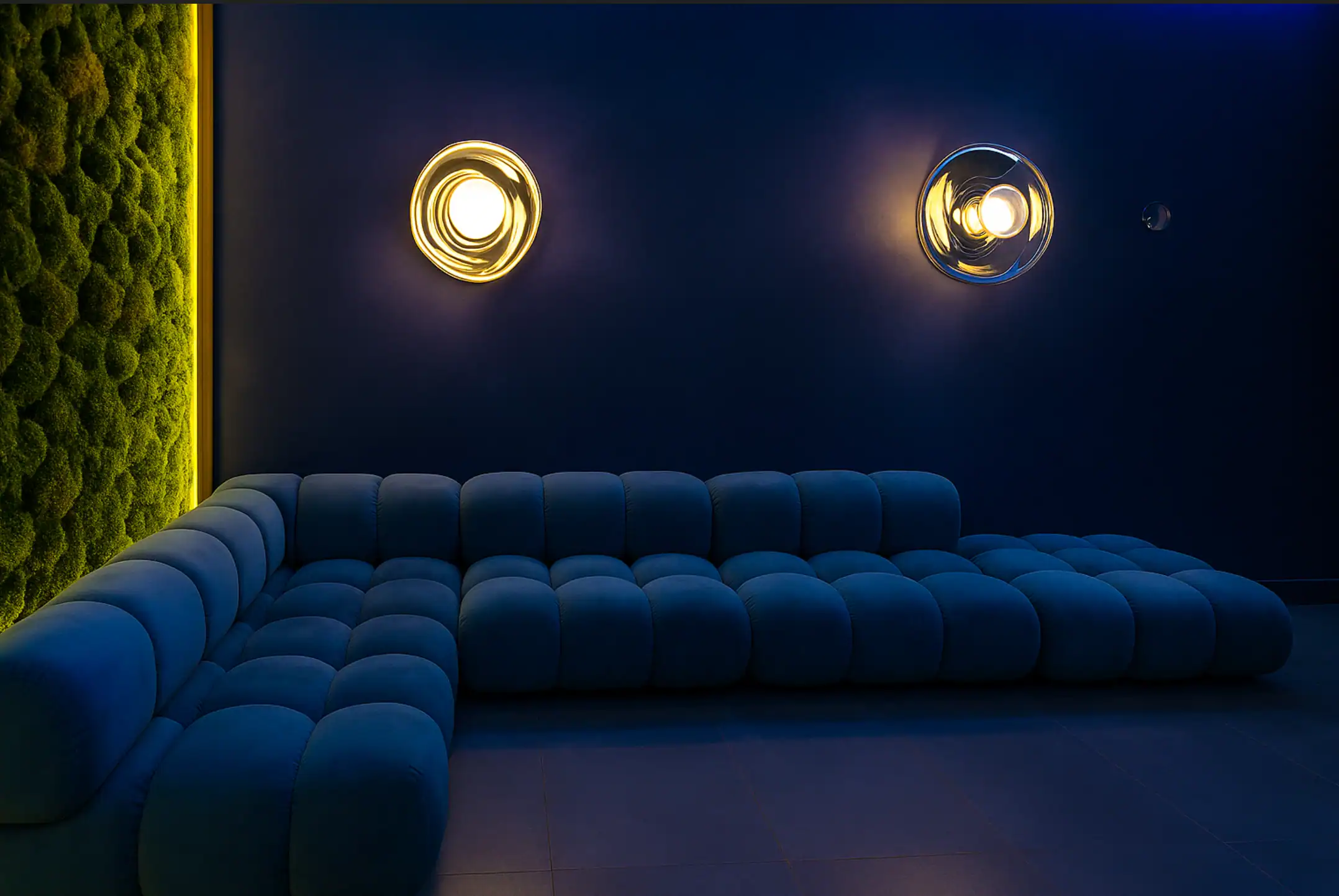 Elegant blue sofa with vibrant lighting and green moss wall in a contemporary interior space.